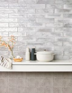 a white counter top sitting next to a bowl and vase with flowers on it in front of a brick wall