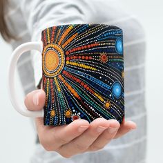 a person holding a coffee mug with an artistic design painted on it's side