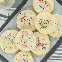 cookies with white frosting and sprinkles on a tray, ready to be eaten