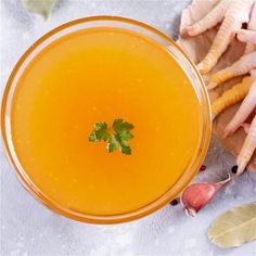 an orange drink in a glass with parsley garnish on the rim next to garlic and ginger