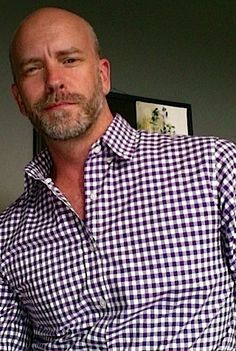 a bald man wearing a blue and white checkered shirt with his hands in his pockets