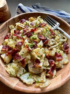 a wooden bowl filled with potato salad next to a fork