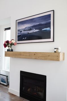 a white fireplace with a wooden mantle and flowers on the mantel shelf next to it