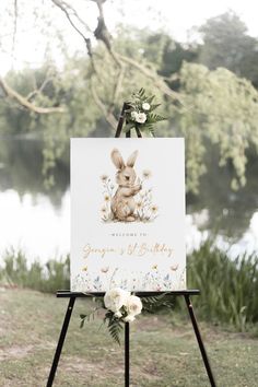 an easel with a greeting card on it in front of a lake and flowers