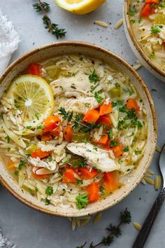 two bowls of chicken noodle soup with lemon and parsley