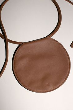 Folded, circular waist bag in saddle brown with two interior slit pockets and magnetic closure. Rolled strap that can be tied and worn multiple ways, at the waist, crossbody, or as a clutch. Unlined, 100% leather. Measures 7" tall, 7.5" wide, strap is 65" long. Handmade in Los Angeles. Circle Bags, Ethereal Elegance, Bags Ideas, Circle Template, Luxury Crossbody, Saddle Brown, Unique Bags, Purse Patterns, Simple Bags