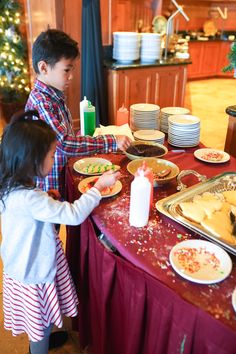 two children standing at a table with food on it and plates in front of them