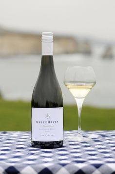 a bottle of wine sitting next to a glass on top of a blue and white table cloth