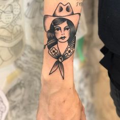 a woman wearing a cowboy hat and holding a pair of scissors on her wrist tattoo