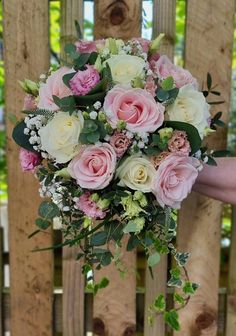 a bridal bouquet with pink and white flowers in front of a wooden fence at a wedding