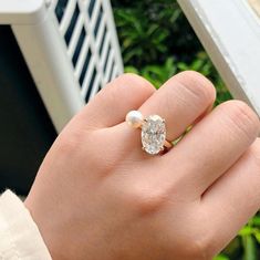 a woman's hand holding an engagement ring with a diamond and pearl on it