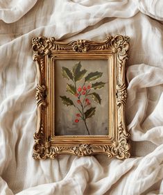 a painting with red berries on it in a gold frame sitting on a white sheet