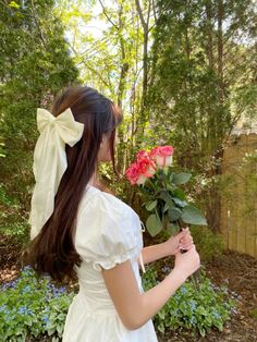 a woman in a white dress is holding a bouquet of roses and looking at it