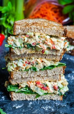 three sandwiches stacked on top of each other with lettuce and tomatoes in the background