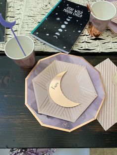 a table topped with plates and cups filled with liquid next to a book on top of a wooden table