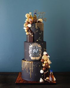 a three tiered cake is decorated with gold and black confetti, liquor bottles, and balloons