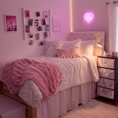 a bed with pink blankets and pillows in a room that has pictures on the wall