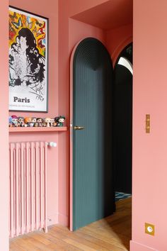 an open door in a pink room with artwork on the wall and wooden flooring