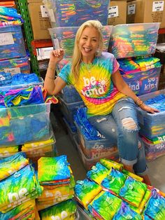 a woman sitting on top of boxes filled with colorful items in a room full of cardboard boxes