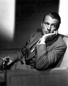 a man in a suit sitting on a couch with his hand under his chin and looking at the camera