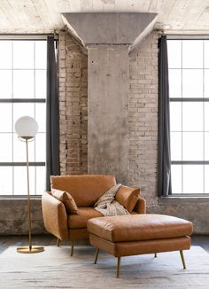 a living room with brick walls and floor to ceiling windows, a leather chair and footstool in front of a large window