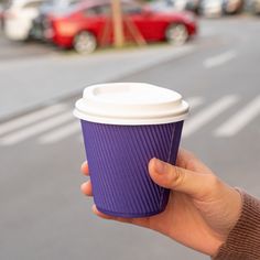 a hand holding a purple coffee cup in front of a street with cars on it