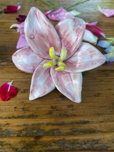 a pink flower sitting on top of a wooden table next to other flowers and petals