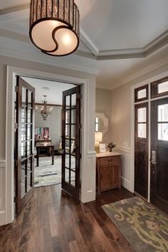 an entry way with wooden floors and two doors leading to another room that has a chandelier hanging from the ceiling