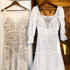 two white dresses hanging up against a wall next to each other on wooden hangers