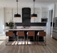 a large kitchen with white cabinets and black counter tops is seen in this image, there are four chairs at the center of the island