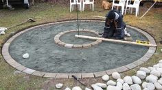 a man kneeling down in front of a circle made out of rocks and sticks with a flag on it