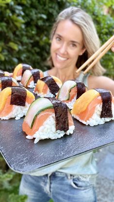 a woman holding a tray with sushi on it and chopsticks in her hand