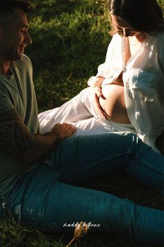 a man and woman sitting on the grass together smiling at each other's eyes