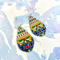 two pairs of colorful earrings sitting on top of a blue and white background with watercolor paint