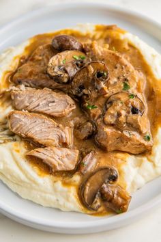 mashed potatoes topped with meat and mushrooms in gravy on a white plate