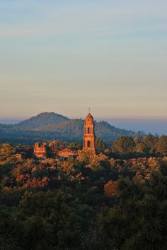 an old church sits on top of a hill surrounded by trees and mountains in the distance