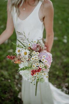 a woman in a white dress holding a bouquet of wildflowers and daisies