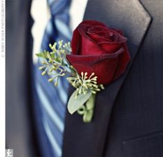 a boutonniere with a single red rose attached to the lapel of a suit