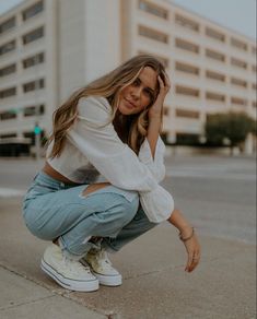 a woman kneeling down on the sidewalk with her hand under her head and looking at the camera