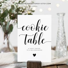 a card with the words cookie table written in cursive writing on it, next to a vase filled with baby's breath flowers