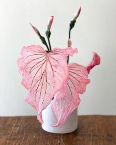 a pink flower in a white vase on a wooden table