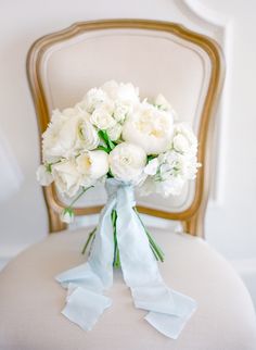 a bouquet of white flowers sitting on top of a chair with blue ribbon around it