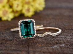 an emerald colored stone surrounded by diamonds on top of a wooden surface with flowers in the background