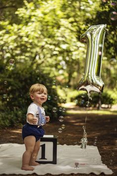 a little boy standing on top of a white blanket next to a number one balloon