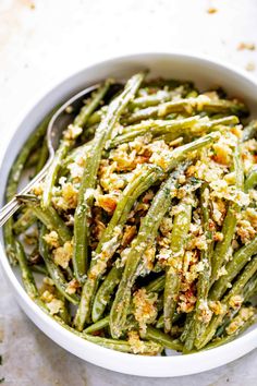 a white bowl filled with green beans covered in crumbled breadcrumbs