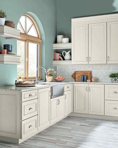 a kitchen with blue walls and white cabinets is pictured in this image, there are plants on the window sill