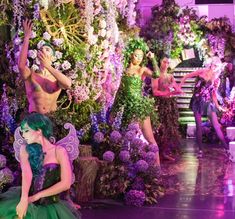 a group of people dressed in fairy costumes dancing on stage with flowers all around them