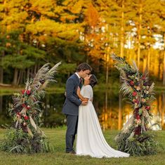 a bride and groom standing in front of an arch decorated with flowers, feathers and foliage