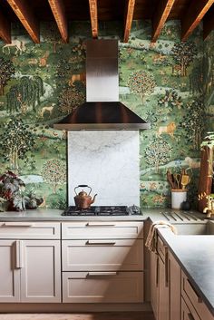 a kitchen with green wallpaper and white cabinets, an oven hood over the stove