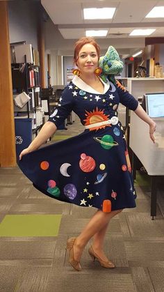 a woman in a dress with planets on it and her hands behind her back, posing for the camera